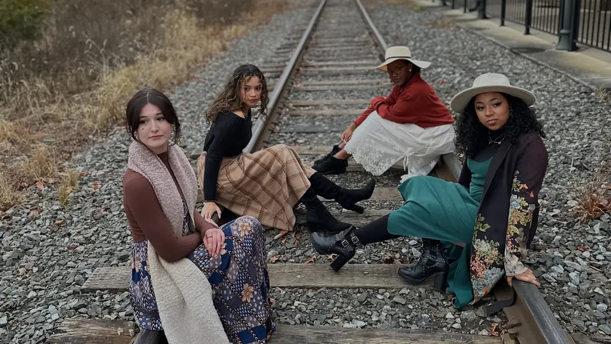 A group of women in vintage-inspired autumn outfits and hats sitting together on old railroad tracks.